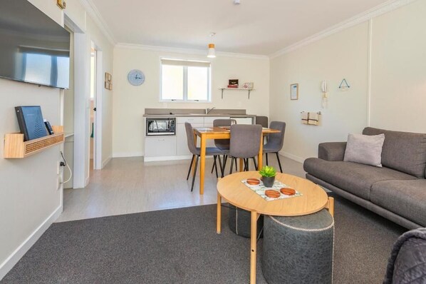 A modern living room with a grey sofa, a wooden coffee table with a plant, and a dining area with a table and chairs. - Kings Court Motel (Whanganui)