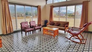 A spacious room with large windows, a patterned floor, a sofa, two armchairs, and a rocking chair.