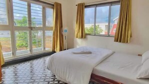 A hotel room with a bed, a window with curtains, and a view of greenery outside.