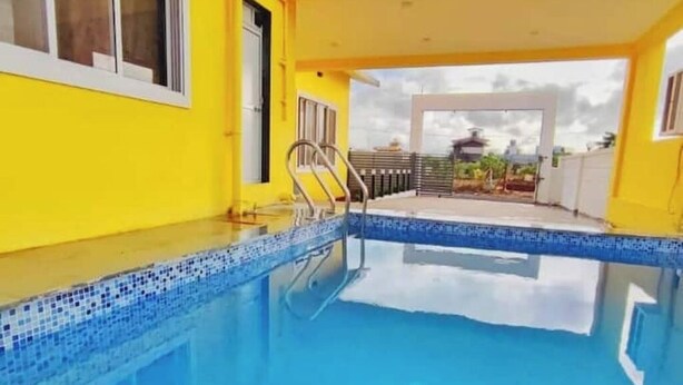 A swimming pool with a tiled edge, a metal ladder, and a view of a building with a yellow facade.