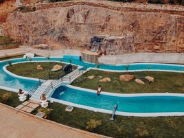 A swimming pool with a waterfall feature, surrounded by grass and rocks.