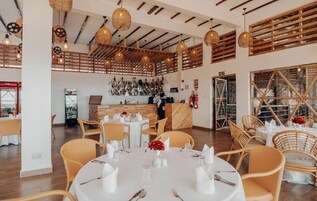 A restaurant with round tables, wicker chairs, and hanging wicker lamps.