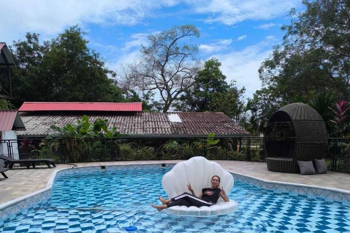 Ein Schwimmbecken mit Kachelmuster, eine Liege und ein überdachter Sitzbereich.