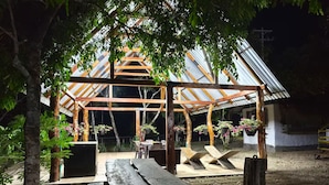 Un kiosque en bois surmonté d’un toit en métal, entouré d’arbres et de plantes en pot.