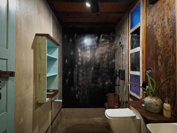 A rustic bathroom with a bathtub, a wooden shelf, a window, and a potted plant. - Svarna (Udupi)