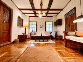 Una habitación con piso de madera, una mesa redonda con sillas, un sofá y un televisor en la pared.