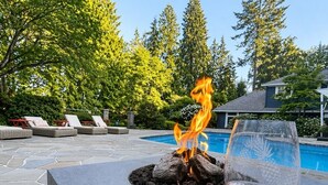 A poolside area with a fire feature and a glass of wine. - World Cup 2026 Luxury Estate, West Van,  Pool, Tennis Court, Theatre, Gym (West Vancouver)