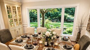 A dining room with a large table set for six, surrounded by chairs, with a view of a garden through large windows. - World Cup 2026 Luxury Estate, West Van,  Pool, Tennis Court, Theatre, Gym (West Vancouver)