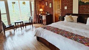 Una camera da letto con un letto grande, pavimento in legno, una scrivania con una sedia, una finestra che si affaccia sul verde e un muro in mattoni.