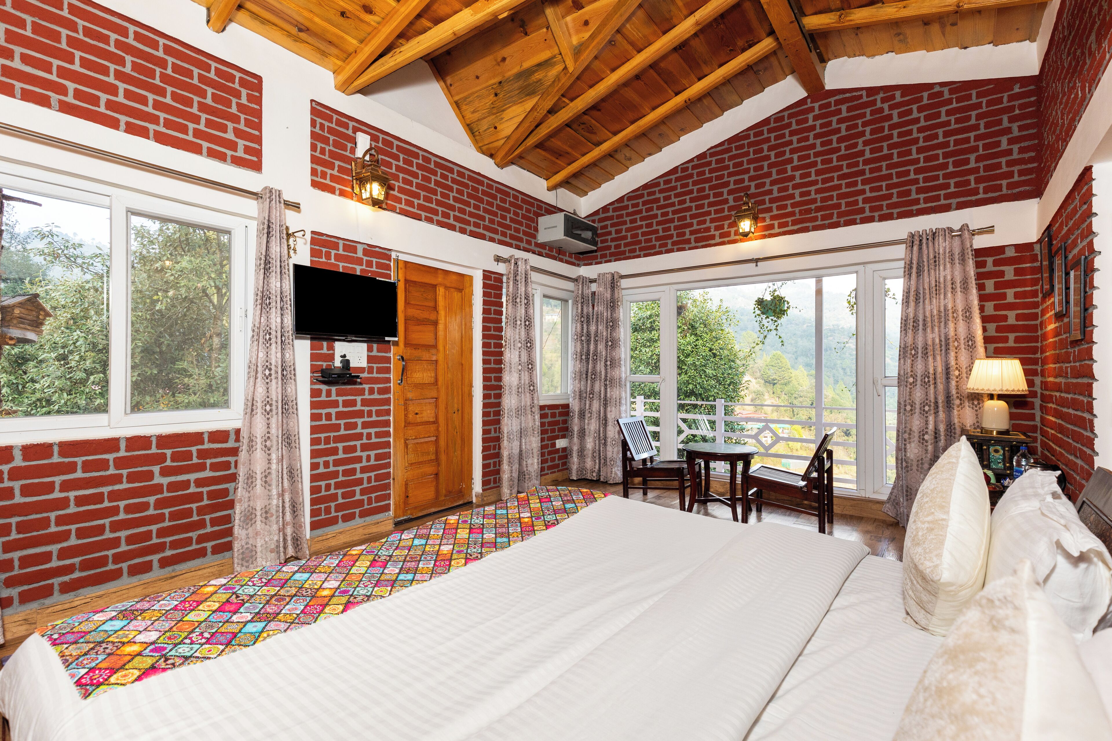 A room with a large bed, a TV mounted on the wall, and a window with curtains.