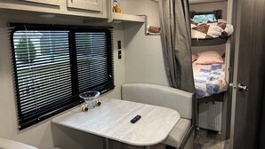Ein kompaktes Wohnmobil-Interieur mit einer Küchenzeile, einem Esstisch, einer Sitzecke und einem Schlafsteige.
