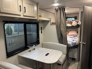 A compact RV interior with a kitchenette, a dining table, a sofa, and a bunk bed. - 4 miles from lake James State Park. Enjoy this brand new camper on private lot. (Nebo)
