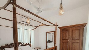 Un letto a baldacchino con struttura in legno e uno specchio sopra. Si nota anche un armadio in legno e una ventola a soffitto nella stanza.