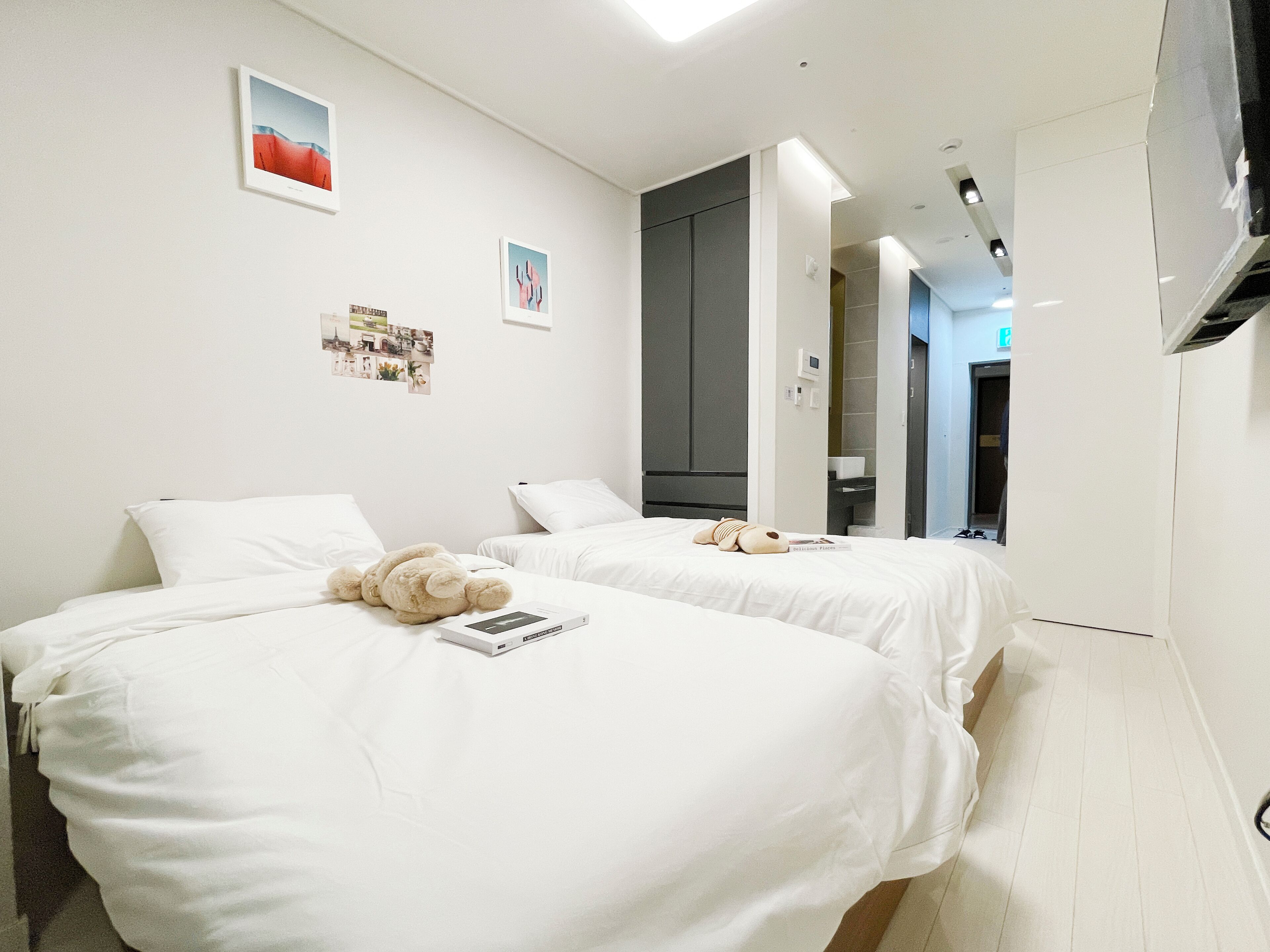 A hotel room with two beds, white bedding, a teddy bear, and a book on the left bed.