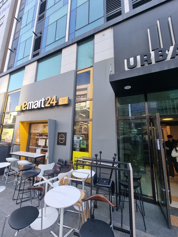 An outdoor seating area with tables and chairs in front of a building with signage for 'emart24' and 'URBAN'. - MZstay Seomyeon (Busan)