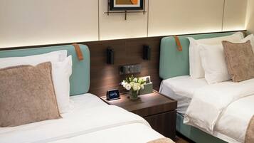 Habitación de hotel con dos camas, una mesita de noche con un reloj y un florero, y un cuadro en la pared.
