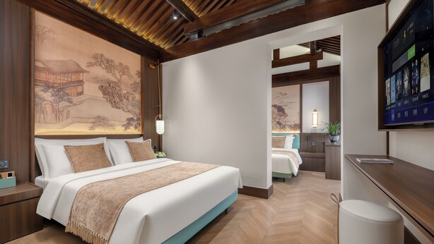 Une chambre d’hôtel moderne, dotée d’un grand lit, d’un bureau, d’une télévision et d’une œuvre d’art traditionnelle accrochée au mur.
