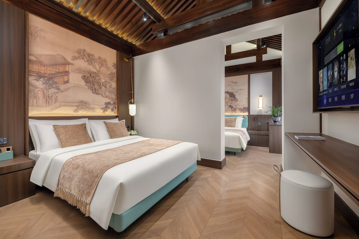 Ein modernes Hotelzimmer mit einem großen Bett, einem Schreibtisch, einem Fernseher und einem traditionellen Kunstwerk an der Wand.