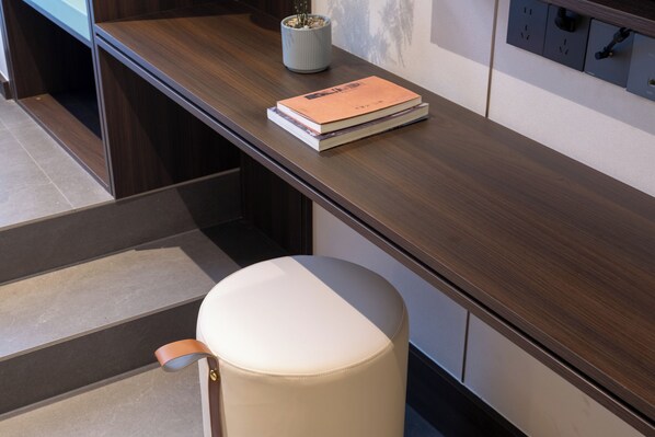 Una habitación moderna con un escritorio de madera, una pila de libros, una planta en maceta y un reposapiés blanco.