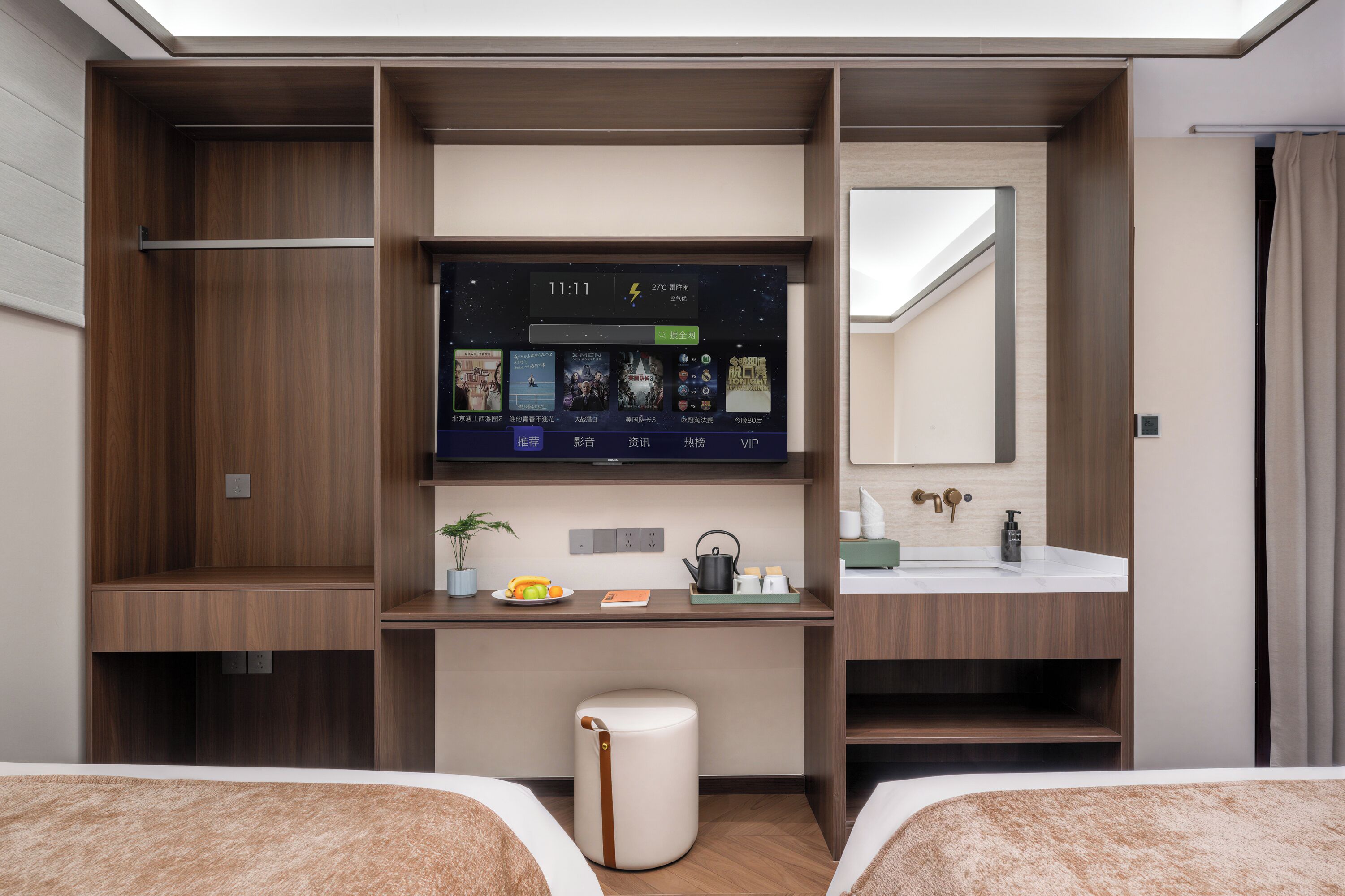 A hotel room with a TV, a desk with a plant, a small stool, a mirror, and a bed.