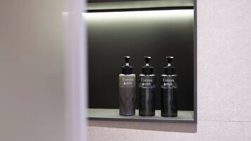 Un baño con espejo, tres botellas de Enroya y una repisa iluminada.