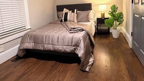Quarto com cama, ventoinha no teto, mesa de cabeceira, abajur e planta em vaso.