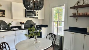 A modern kitchen with white cabinets, a black countertop, a round dining table, and a chandelier. - The Porch Parlor-Historic Oakwood, walkable, Pets (Raleigh)