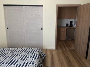 Ein Schlafzimmer mit Bett, Kleiderschrank und einer offenen Tür zu einer Küchenzeile.