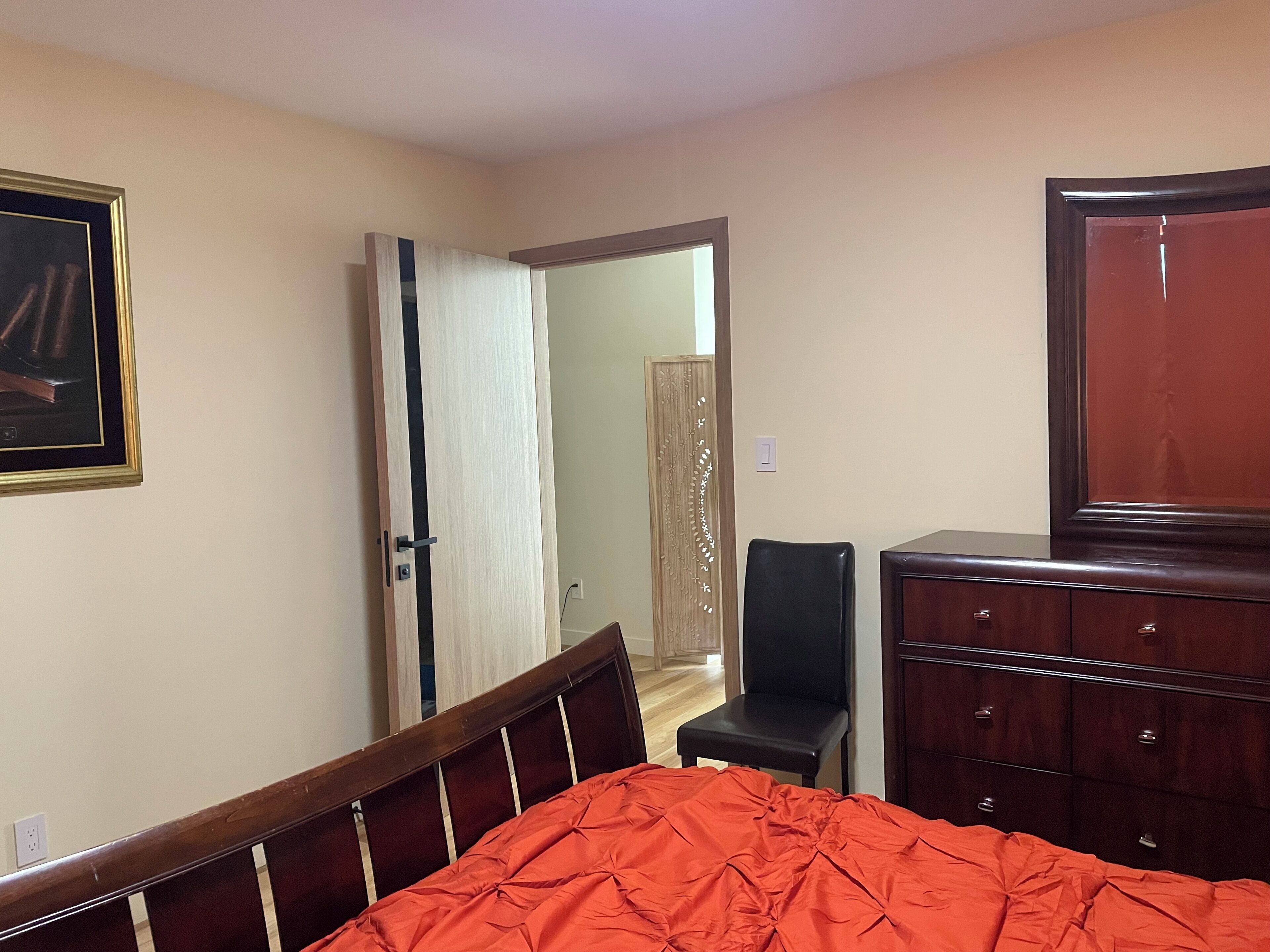 Une chambre à coucher comprenant un lit, une commode, une chaise et une porte donnant sur une autre pièce.