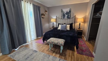 A bedroom with a bed, bedside lamps, a bench, a closet, and a view of a landscape painting.