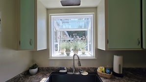 Une cuisine dotée d’une fenêtre, d’un évier, d’un plan de travail en granit et de meubles de couleur verte.