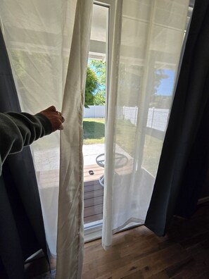 Blick durch ein Fenster mit transparenten Vorhängen, einem Holzboden und einem weißen Zaun im Hintergrund.