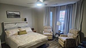 A hotel room with a bed, two armchairs, a desk with a computer, a ceiling fan, and a window with curtains. - 3bd/2bth Home, king/queen bds,crib, RV/trailer parking, pet fence, massage chair (Cabot)