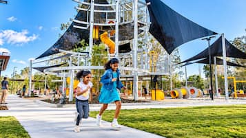 An outdoor playground with a climbing structure and slides, surrounded by a grassy area and trees.