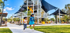 Un espace de jeux extérieur doté d’une structure d’escalade et de toboggans, entouré d’une pelouse et d’arbres.