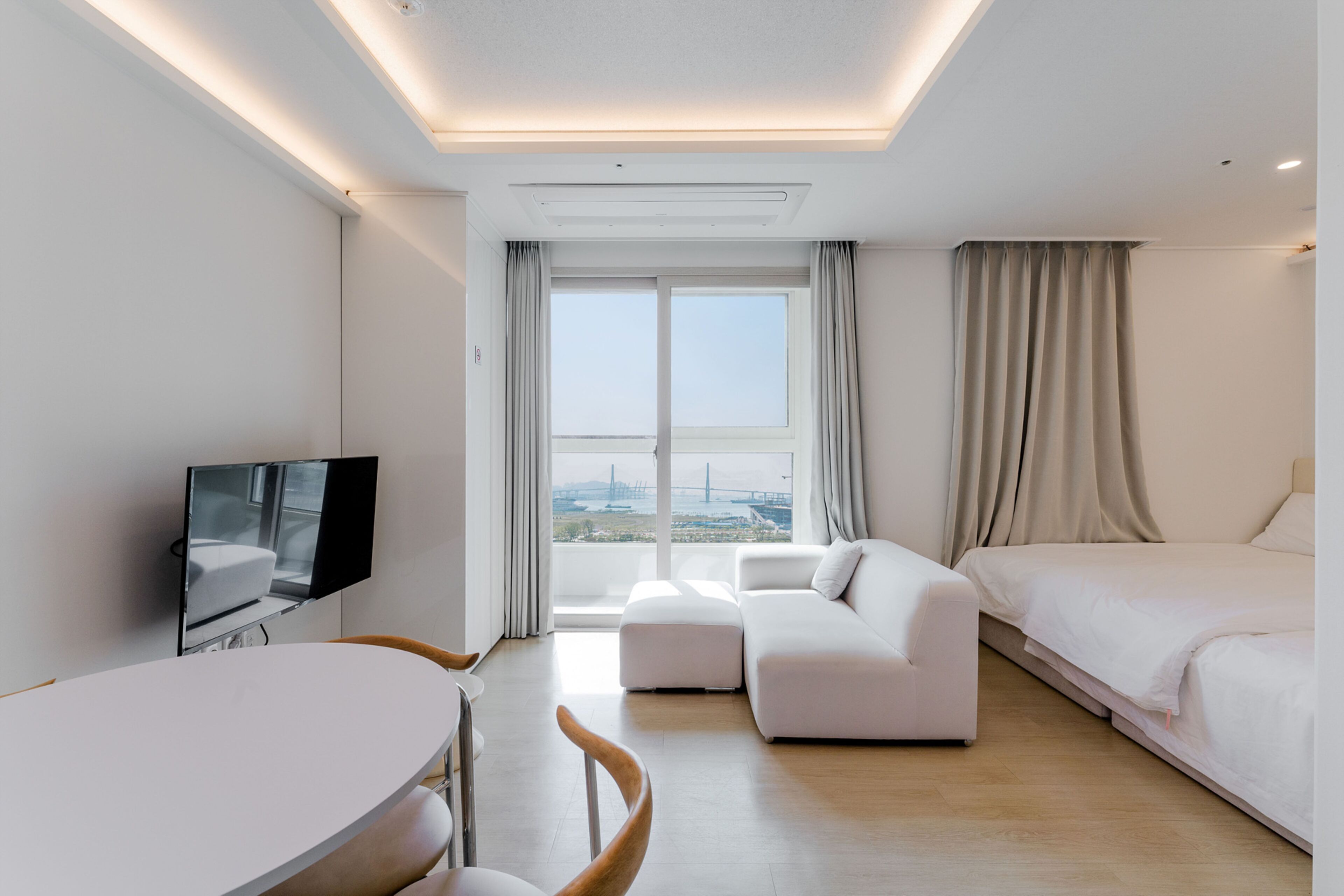 A modern hotel room with a flat-screen TV, a sofa, a bed, and a dining area.