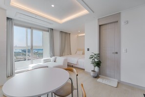 A modern hotel room with a large window, a bed, a seating area with a table and chairs, and a potted plant. - Marant Residence Hotel (Busan)