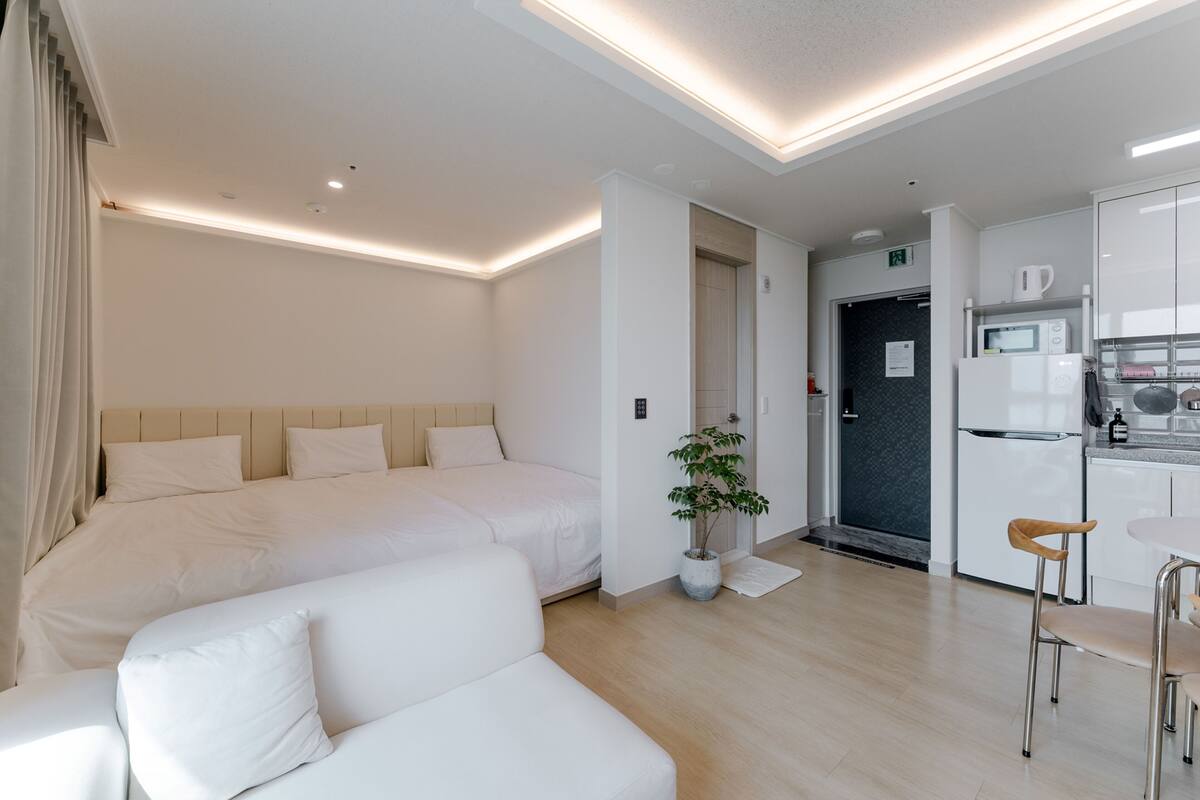 Une chambre d’hôtel moderne avec un grand lit, un canapé, un petit coin cuisine et une plante en pot.