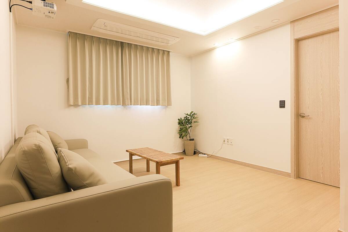 Une pièce comprenant un canapé, une petite table, une plante en pot, une porte et un appareil de climatisation.