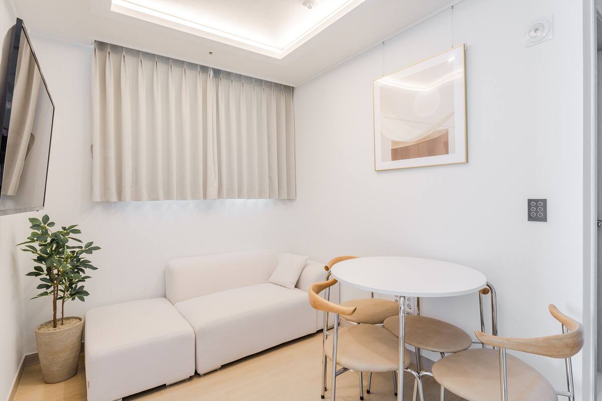 Une pièce moderne avec un canapé blanc, une table ronde et des chaises, une plante en pot et un grand miroir au mur.