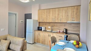 A modern kitchen with wooden cabinets, a microwave, and a sink. There is a dining table with chairs and a fruit bowl. - Happy Stay Apartment By The Sea 094 (Golem)