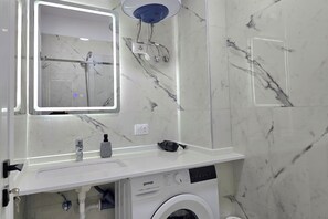 Ein modernes Badezimmer mit einem weißen Marmorwaschbecken, einer integrierten Waschmaschine und einer Handbrause.