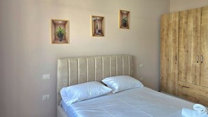 A bedroom with a bed, a wooden wardrobe, and three wall-mounted shelves with plants. - Happy Stay Apartment By The Sea 094 (Golem)