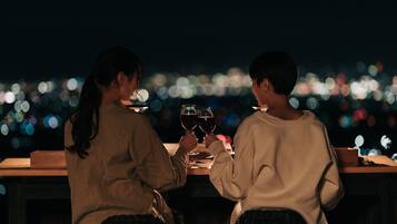 Two people sitting at a table with wine glasses, overlooking a cityscape at night.