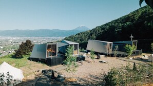Una moderna baita minimalista con un'ampia vetrata, immersa nel verde con una montagna sullo sfondo.