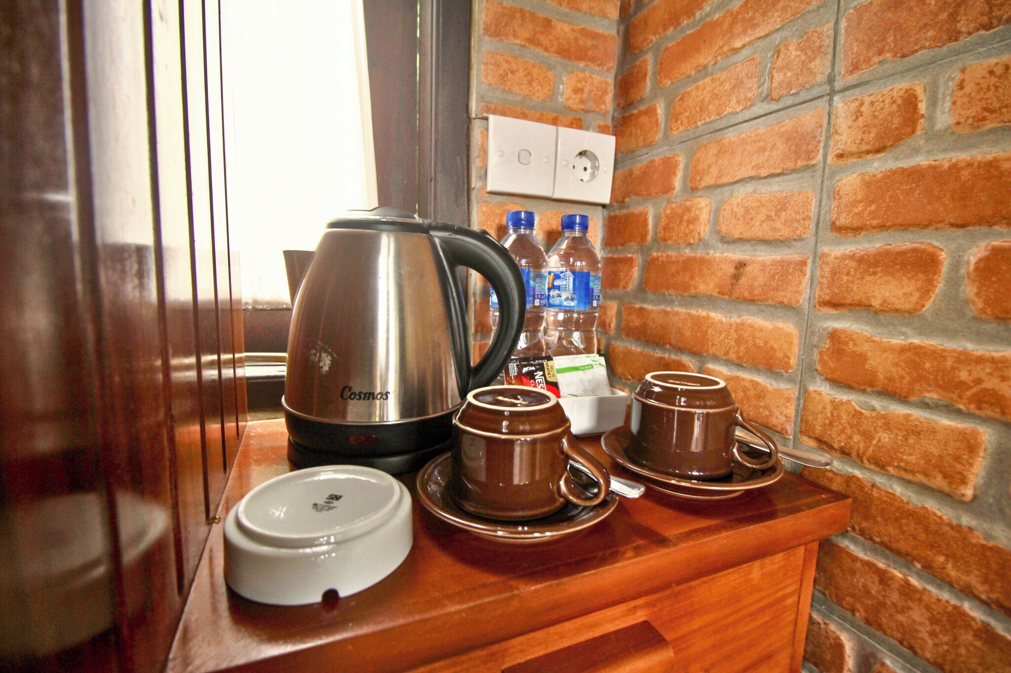 Une petite cuisine équipée d’une machine à café, de deux tasses et d’une bouilloire, le tout posé sur un comptoir en bois.