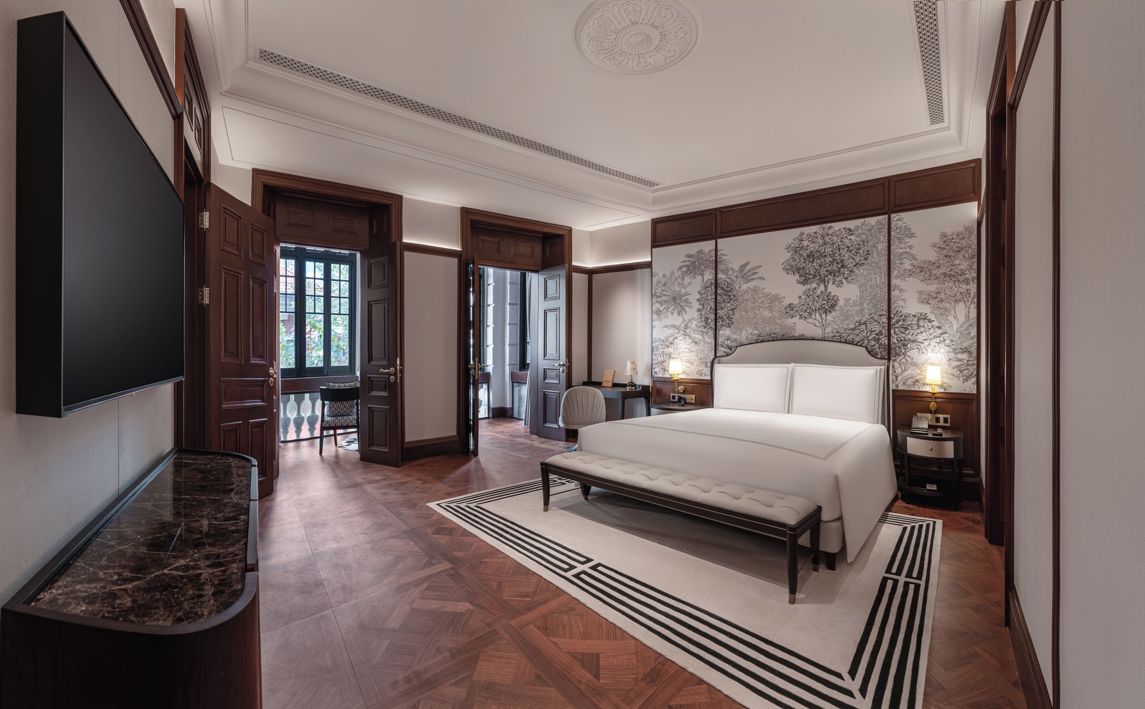 A spacious bedroom with a large bed, a flat-screen TV, a desk, and a chair.