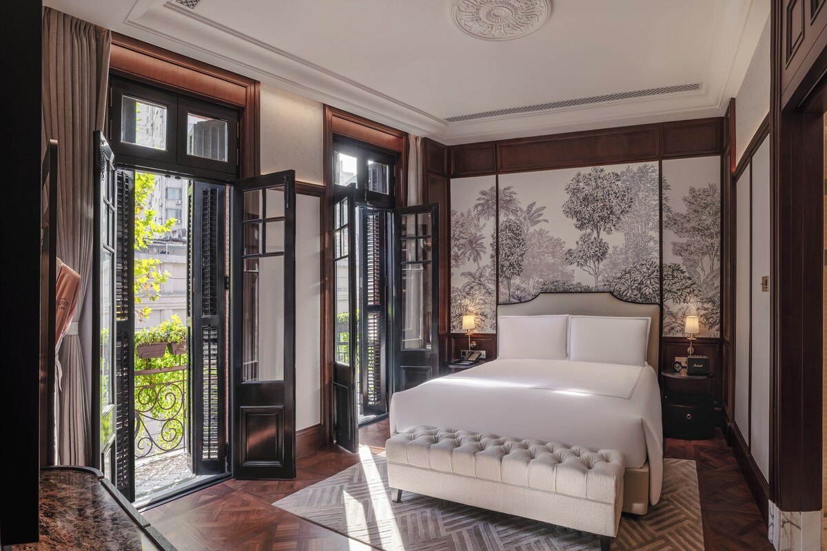 Un dormitorio espacioso con una cama grande, vistas al exterior a través de puertas abiertas y un mural decorativo en la pared.