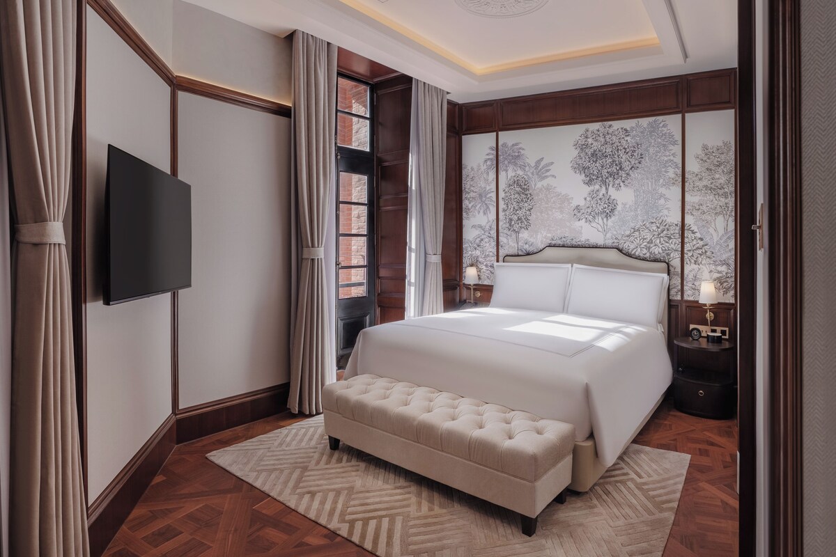 Un dormitorio con una cama grande, televisor, mesita de noche y decoración en la pared.