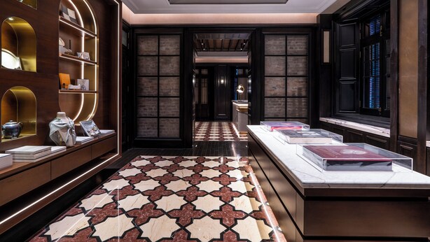 Un moderno vestíbulo de hotel con piso estampado, estanterías de madera con libros y objetos decorativos, y un mostrador de recepción.